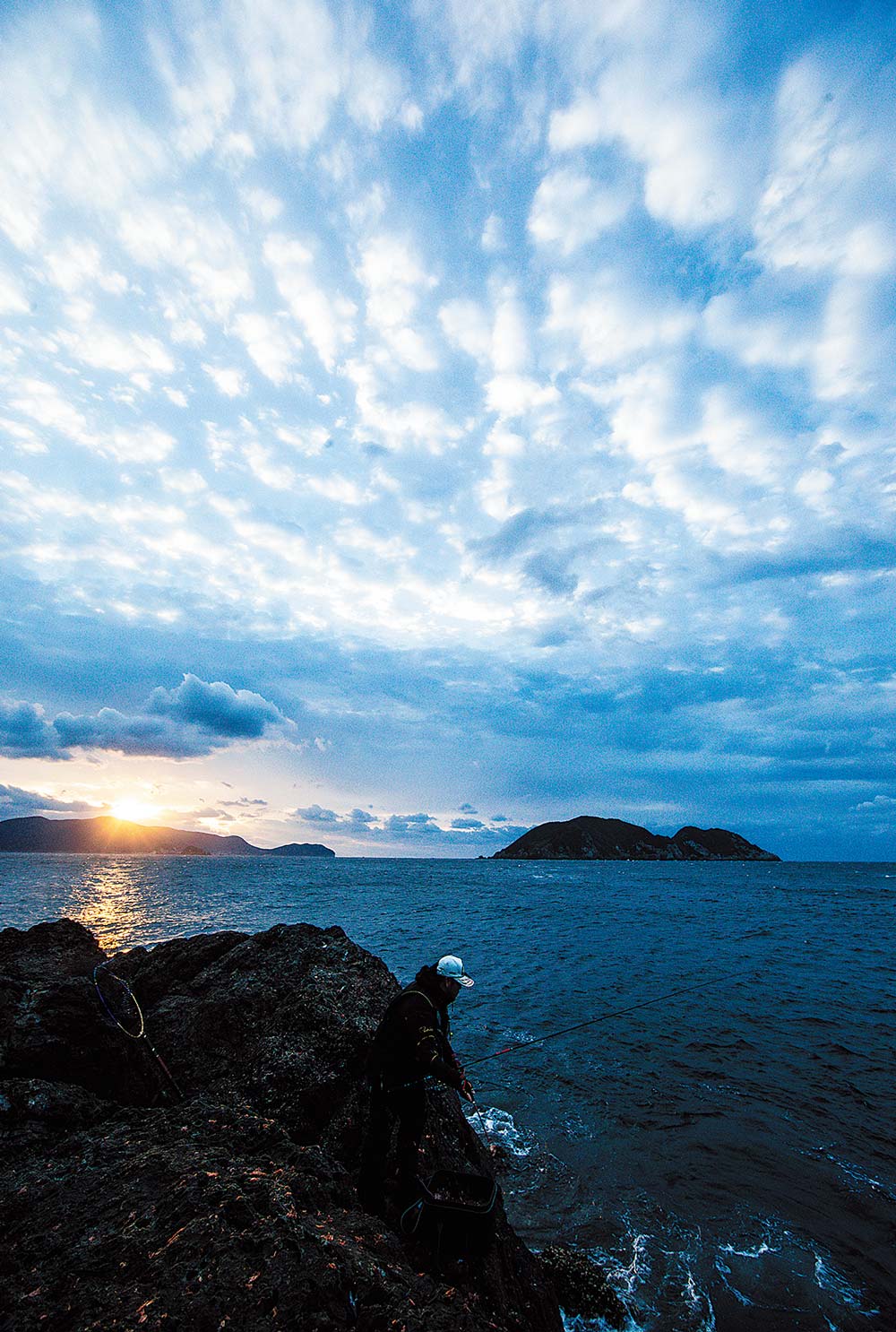 高場で釣りをする山中と、奥に見える沖ノ島から顔を覗かせる朝日