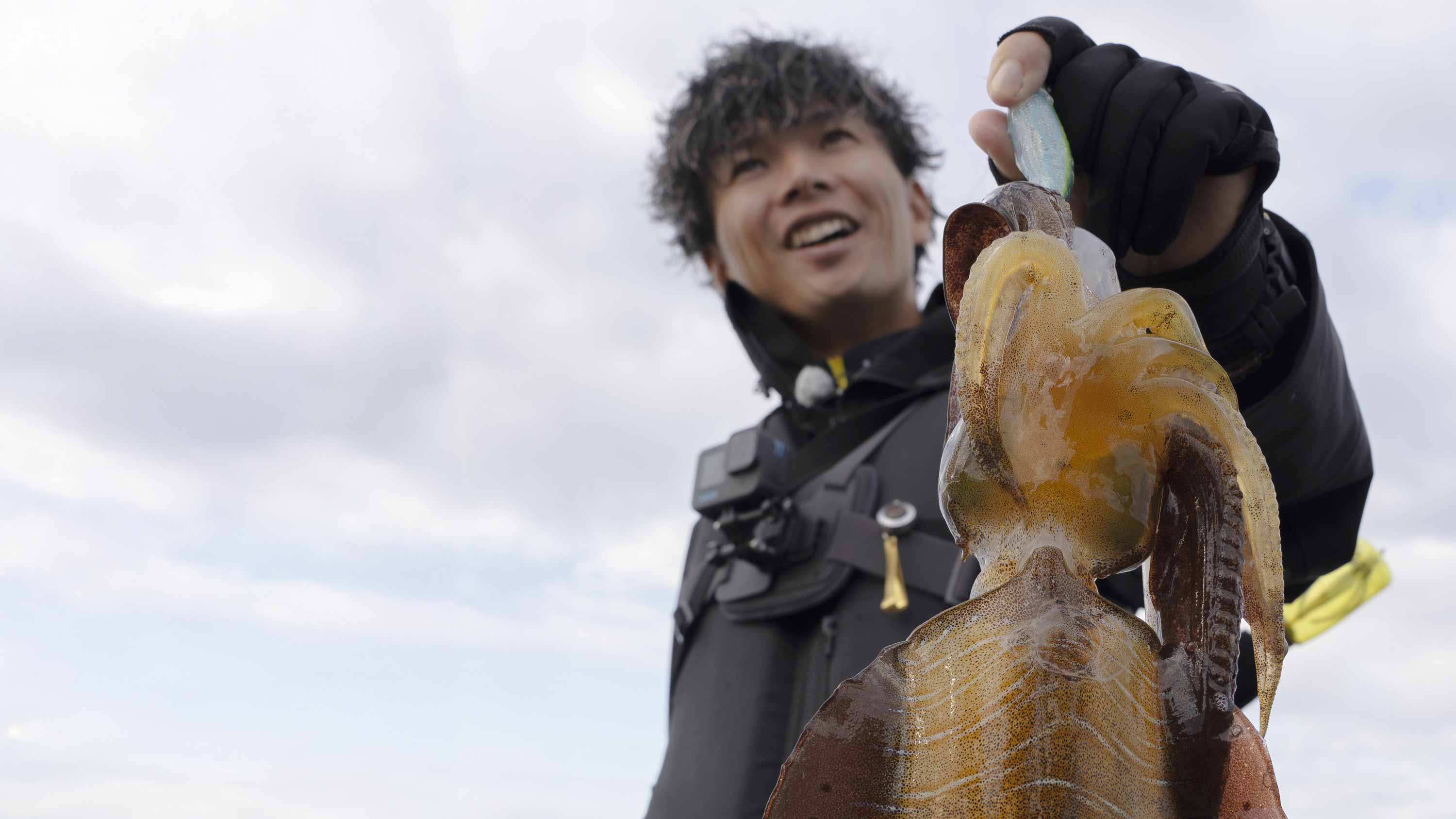 釣り上げたビッグサイズのアオリイカを掲げ、笑顔を見せる勝股