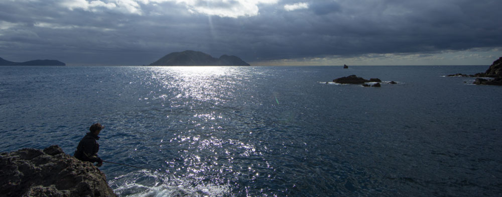 手前の磯で尾長グレを狙う北村。その奥正面には姫島、左沖に沖ノ島、右沖に台形の磯・マルサゲが見える。