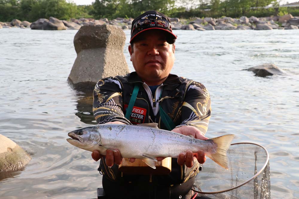 川を背に、釣り上げたサクラマスを両手で持つ長谷川