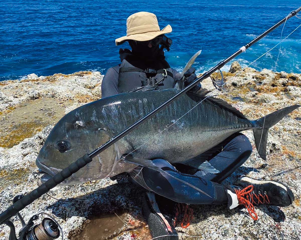 釣り上げた大魚を、胡座をかいた両膝に乗せているアングラー