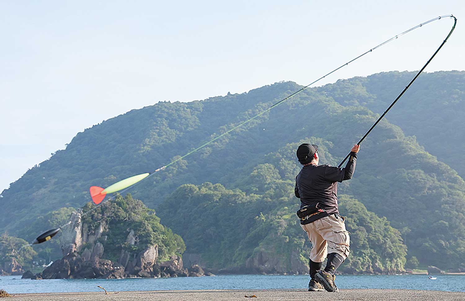 大きく振りかぶり、海へキャストするアングラーの写真