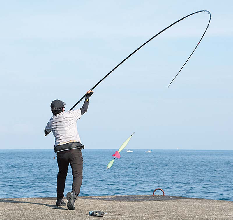 大きく振りかぶり、海へキャストするアングラーの写真