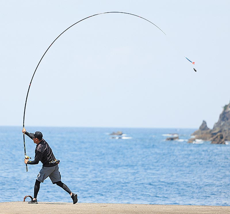 大きく振りかぶり、海へキャストするアングラーの写真