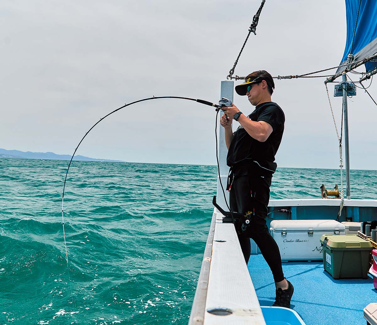 海の船上。力を込め、魚が掛かった竿を引くアングラー。